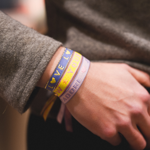 Poignet portant des bracelets en tissu colorés avec messages, dont un bracelet brodé Ambrée