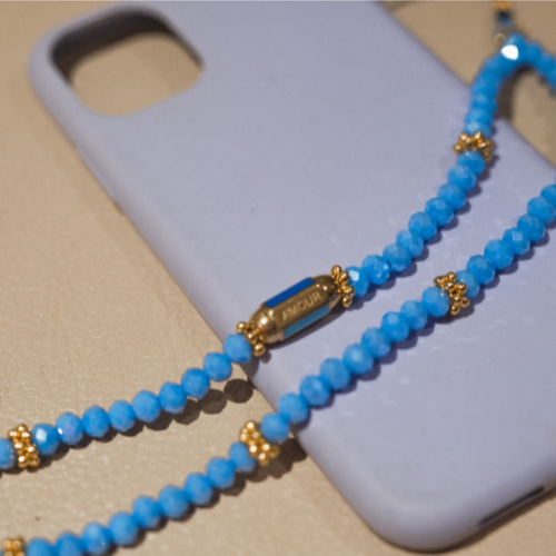 Cordon de téléphone perlé bleu avec détails dorés, posé sur une coque violette