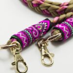 Gros plan sur les embouts brodés du cordon Ambrée rose et beige avec motifs fuchsia, violets et mousquetons dorés